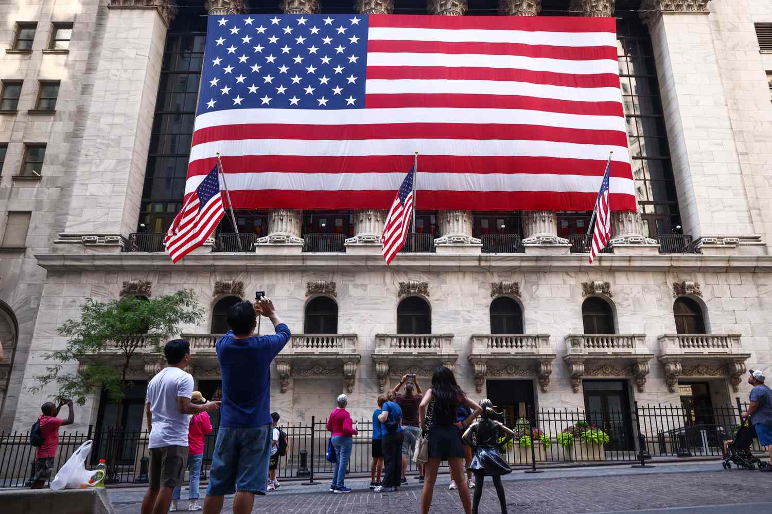 People take pictures of large American flags hanging outside the New York Stock Exchange on July 4