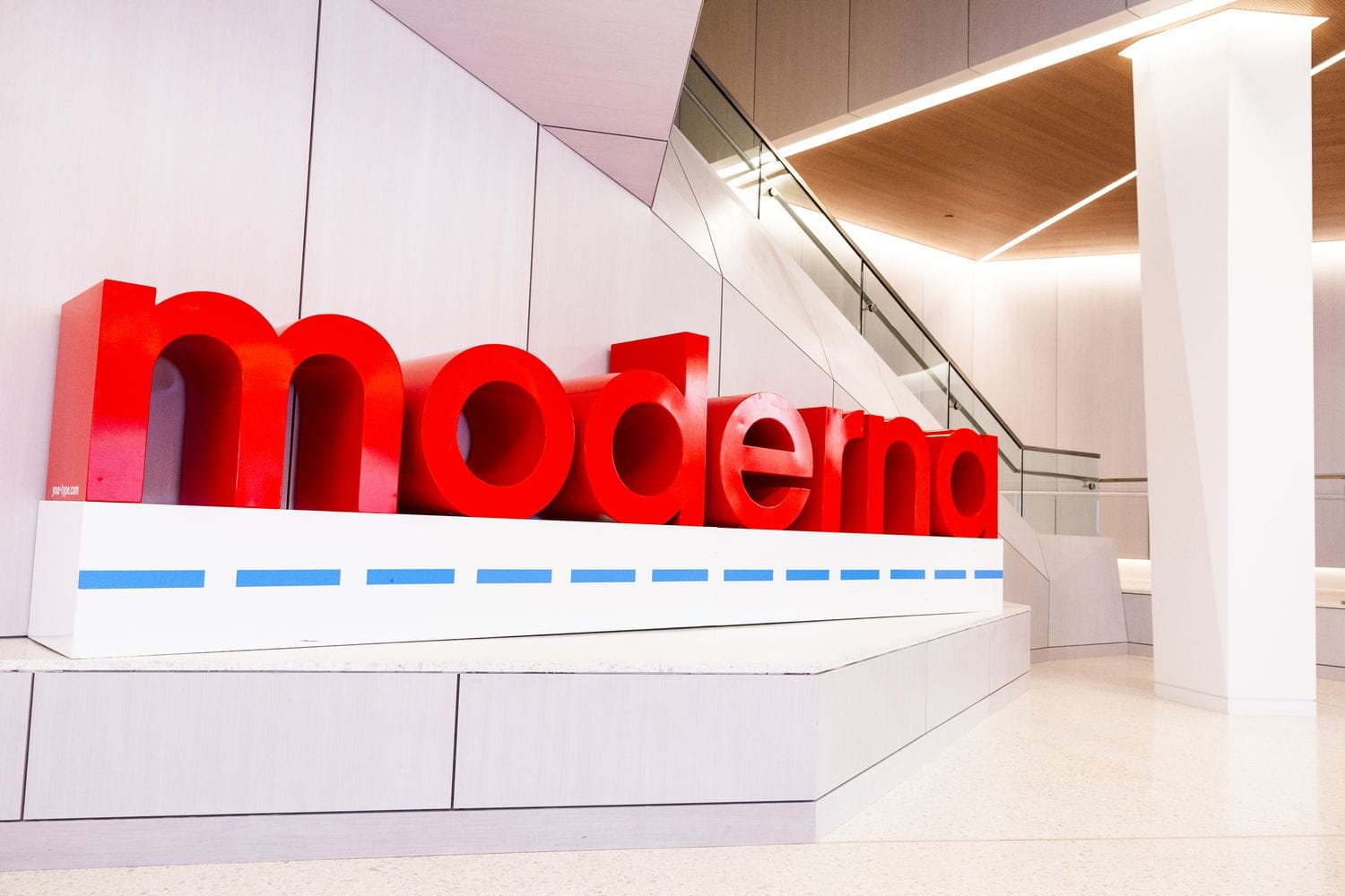 A red Moderna sign is seen inside a white building.