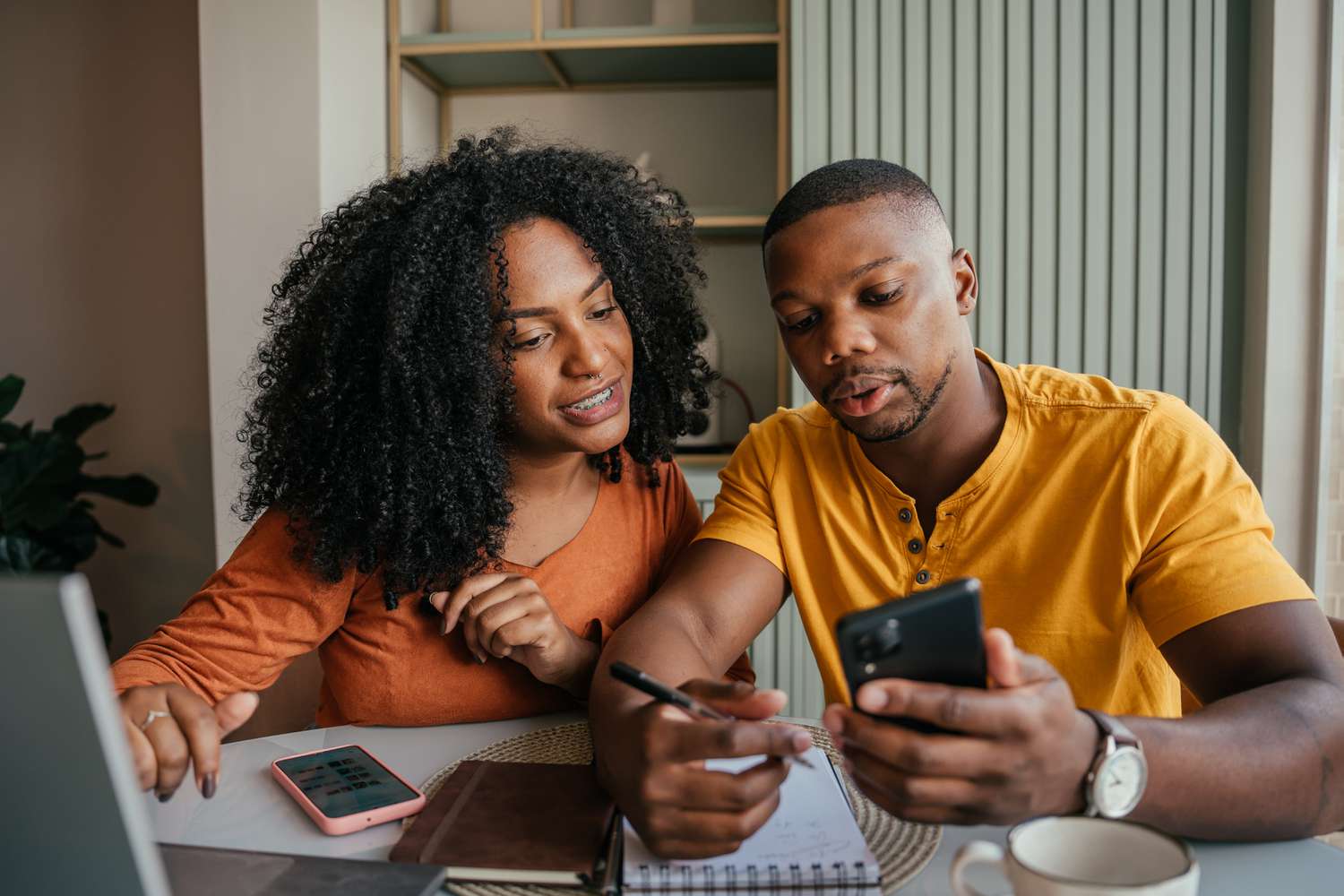 Young couple sitting at kitchen table and looking together at a laptop and smartphone