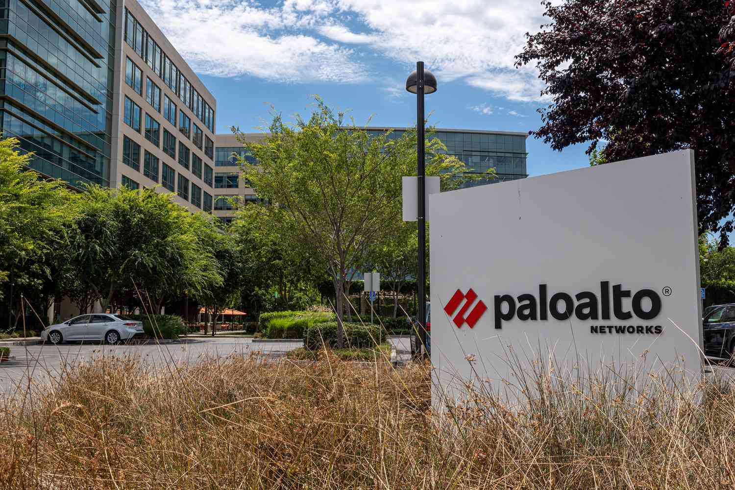 The Palo Alto Networks logo on a sign outside the company's headquarters, with trees and bushes also visible.