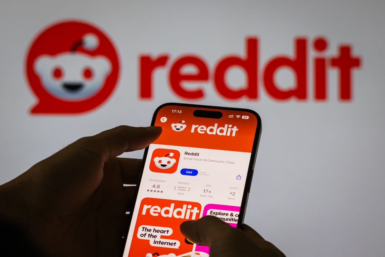 The Apple App Store listing for Reddit is shown on a phone screen in front of a white background also displaying the Reddit logo.