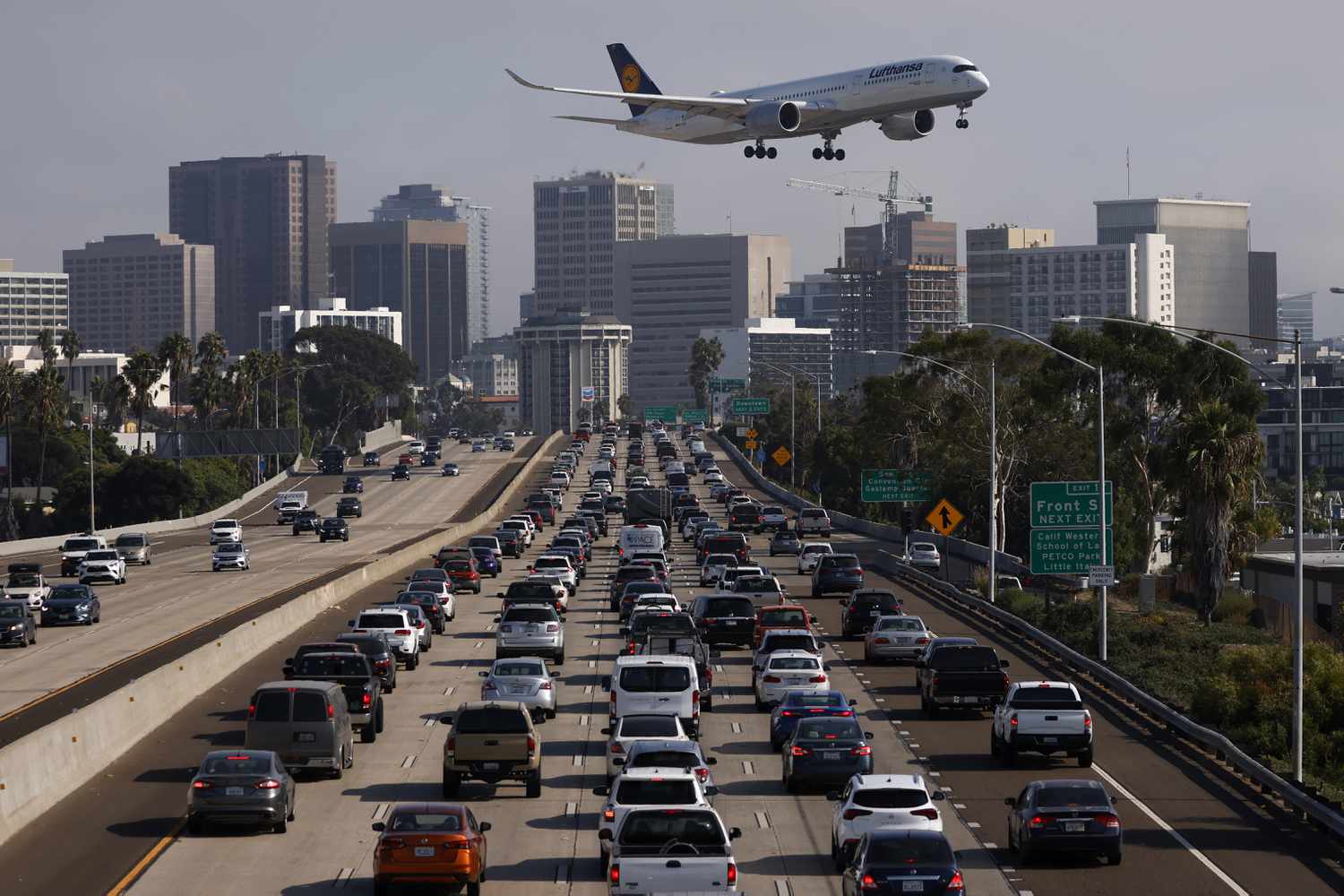 A plane comes in for a landing above a busy highway with cars driving toward a city