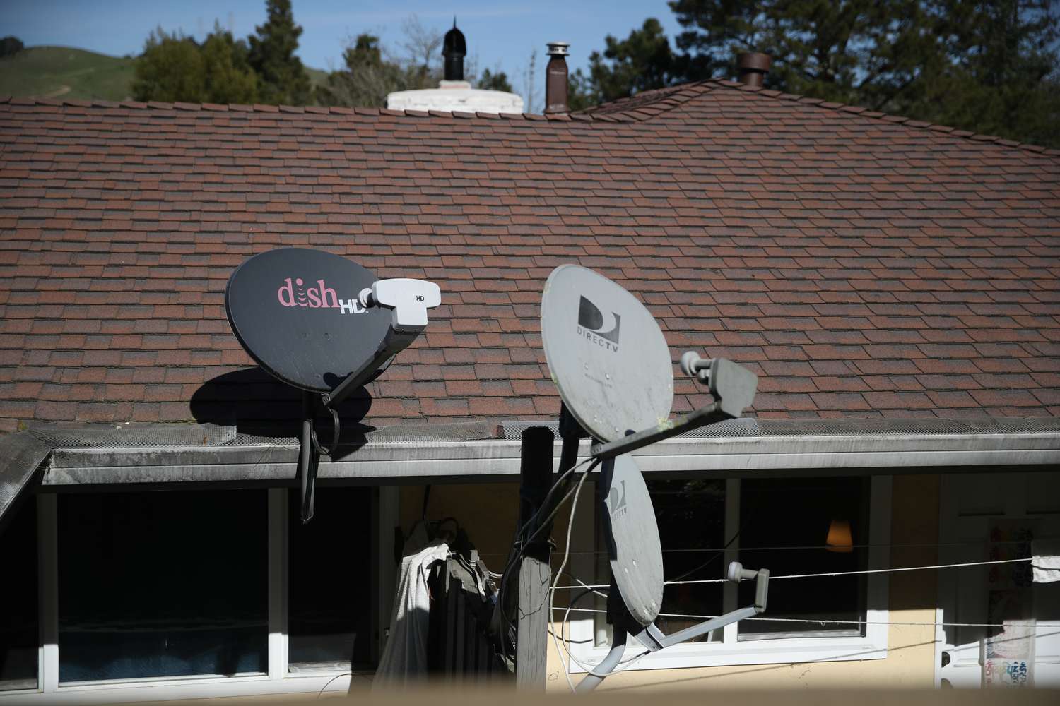 A Dish Network satellite dish is mounted next to a DirecTV dish on the roof of an apartment building in Mill Valley, California