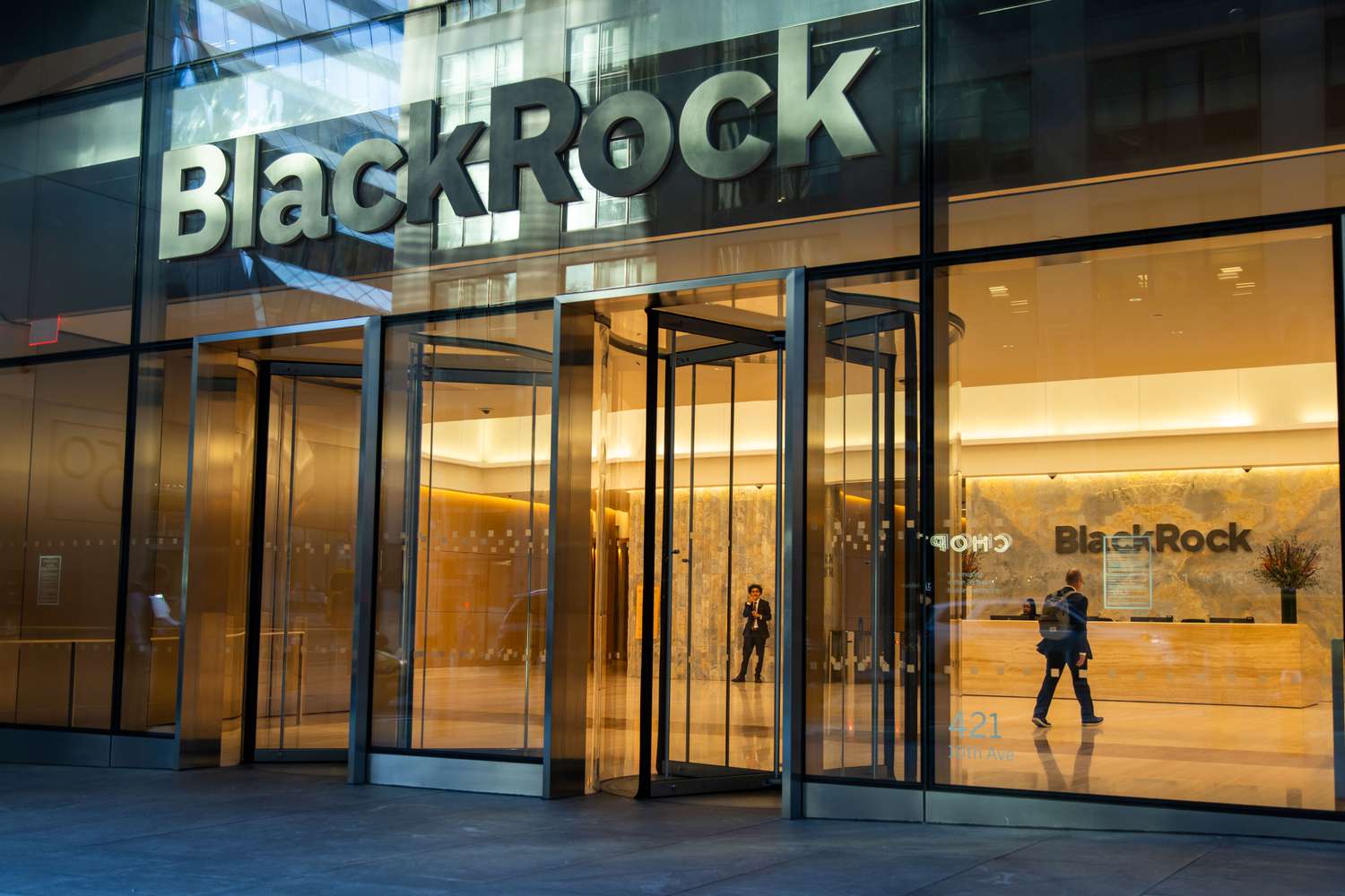 People are seen inside through the windows of BlackRock's headquarters in New York City, with the BlackRock logo above the entrance.