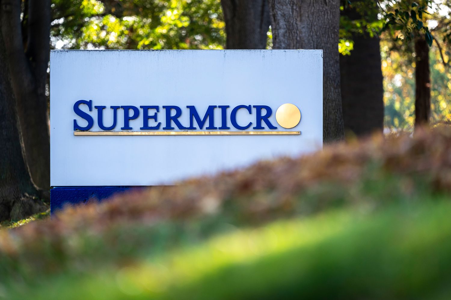 A white sign with blue and gold text that says "SuperMicro" is seen with grass and trees surrounding it.