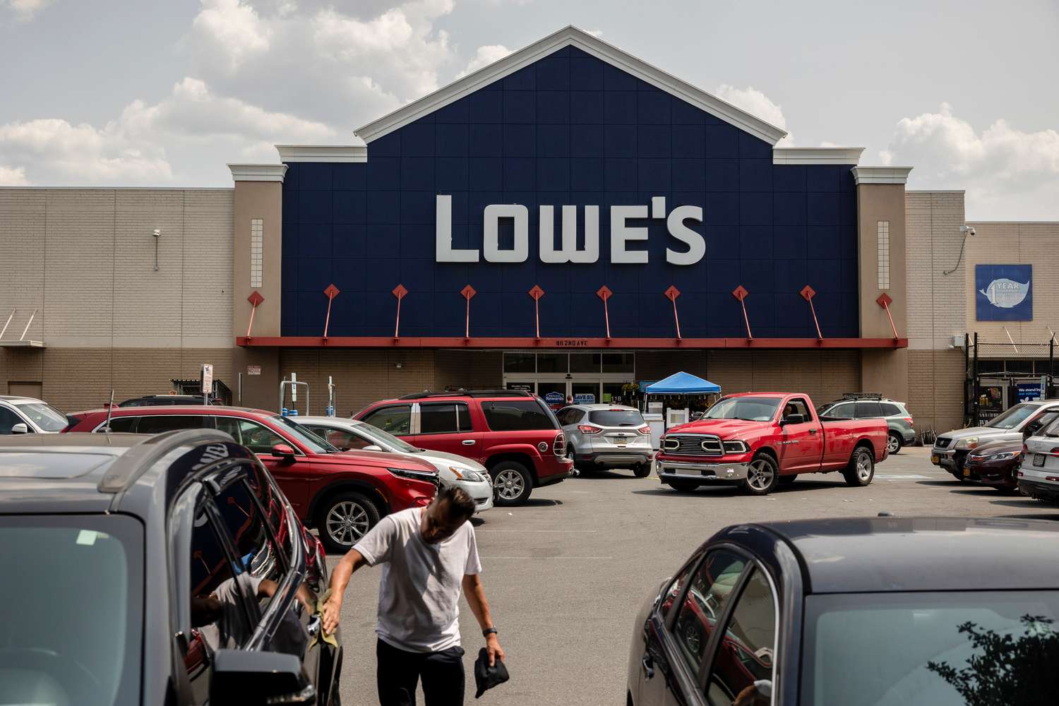 People and cars are seen in a parking lot in front of a Lowe's store.