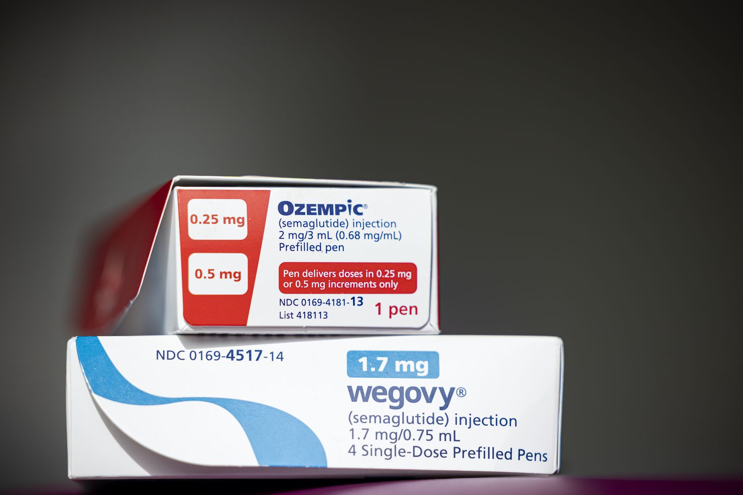 A red and white box of Ozempic is sitting on top of a white and blue box of Wegovy.