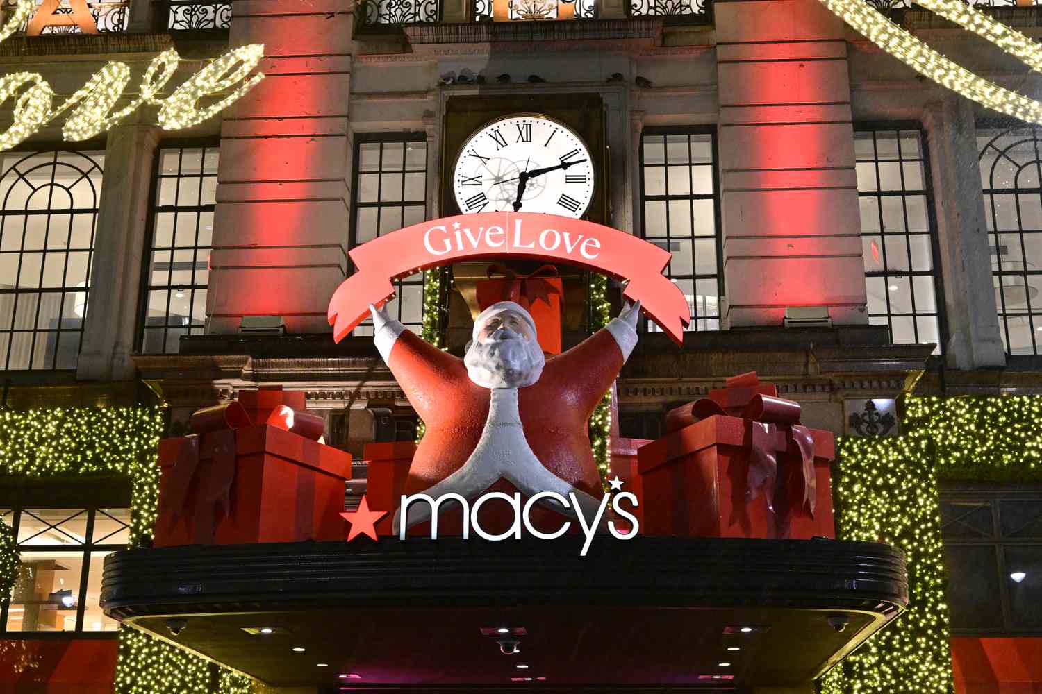 The Macy's logo is seen in front of a building and Santa decoration holding a sign that says "Give Love"