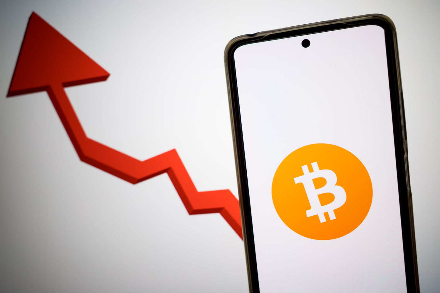 Bitcoin logo on a smartphone next to an up arrow