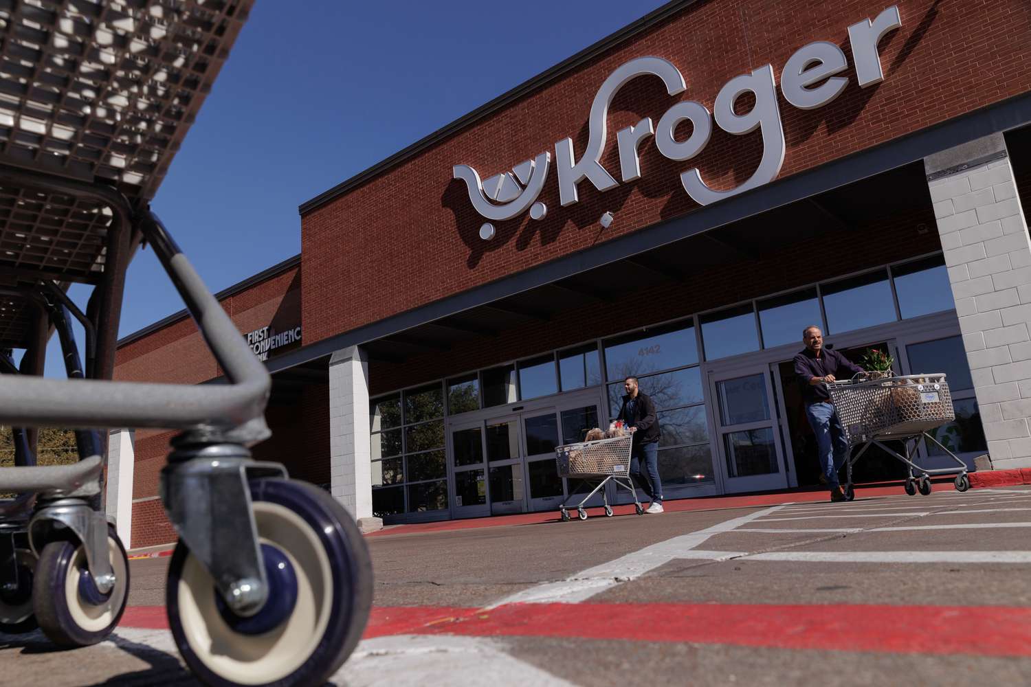 People with shopping carts are seen leaving a Kroger store.