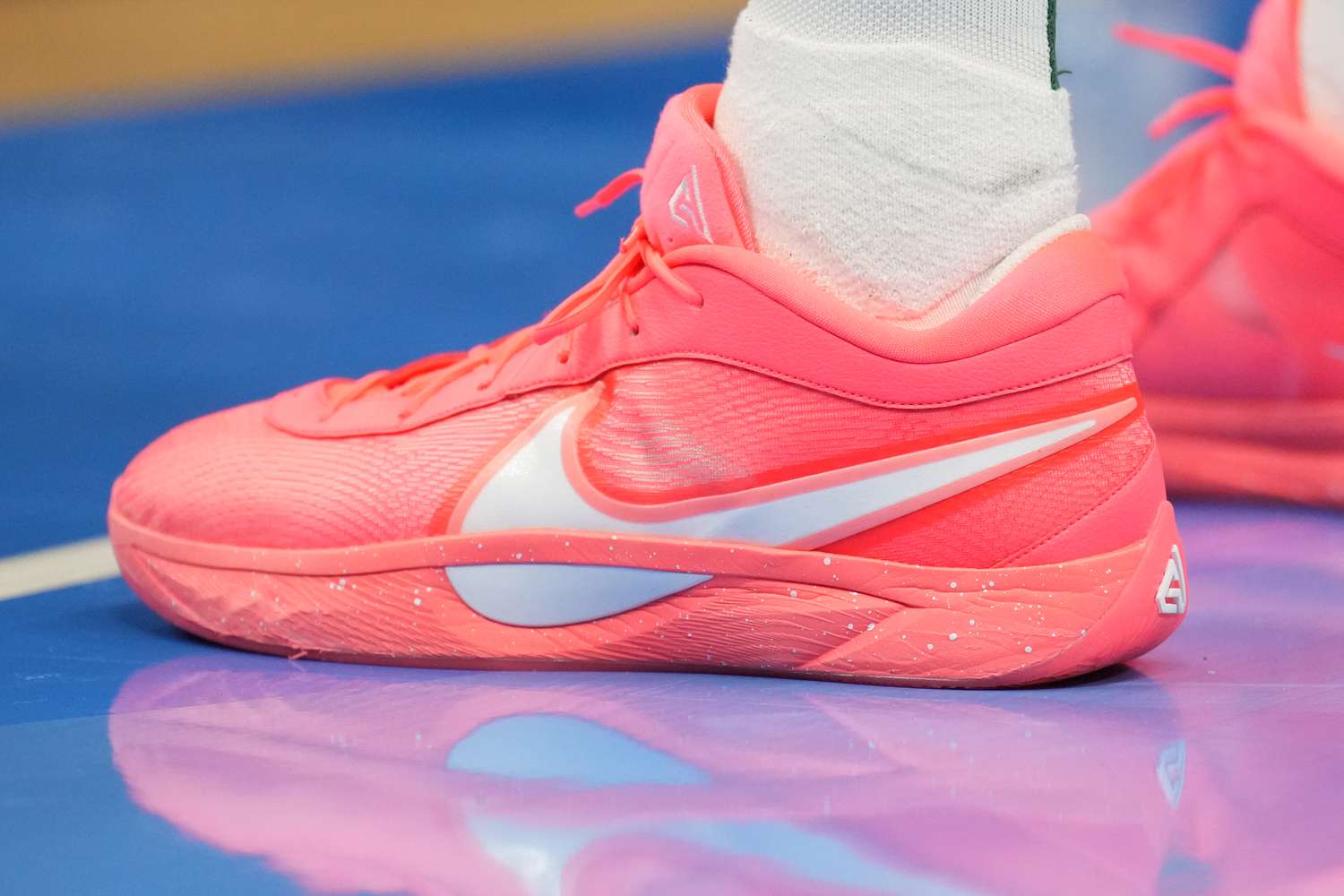 A pair of pink shoes with a white Nike logo are seen on a blue basketball court.