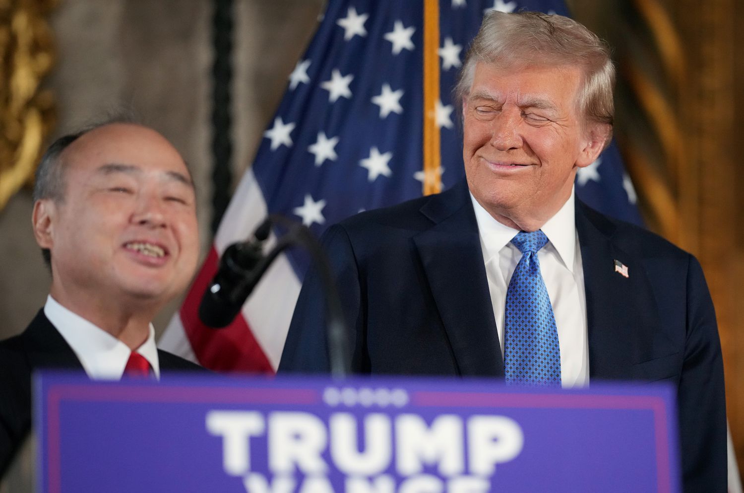 Softbank CEO Masayoshi Son and Donald Trump are seen behind a podium, with part of an American flag visible in the background