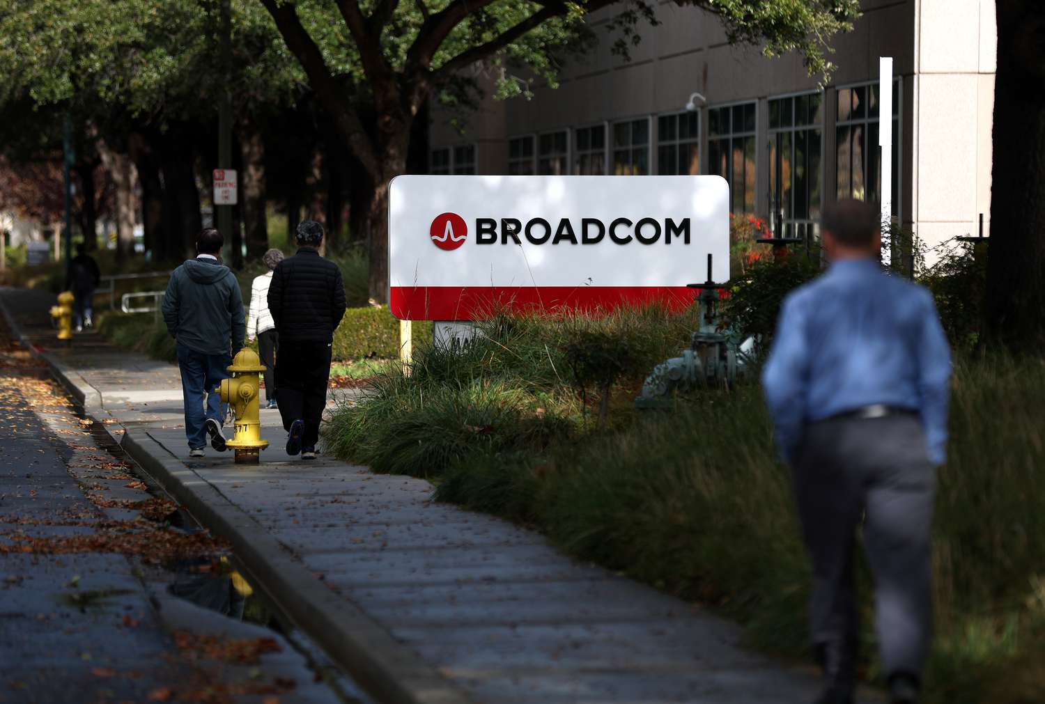 : Pedestrians walk by a sign in front of a Broadcom office on December 12, 2024 in San Jose, California.