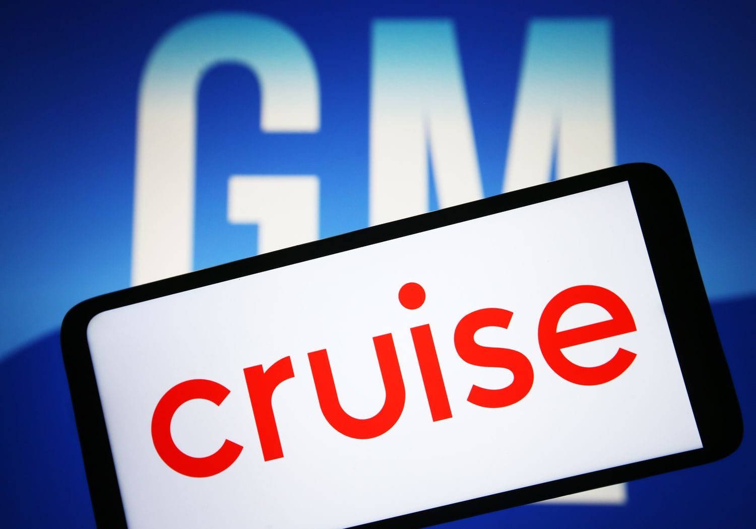 Cruise LLC logo is seen on a smartphone and General Motors Company (GM) logo on a pc screen