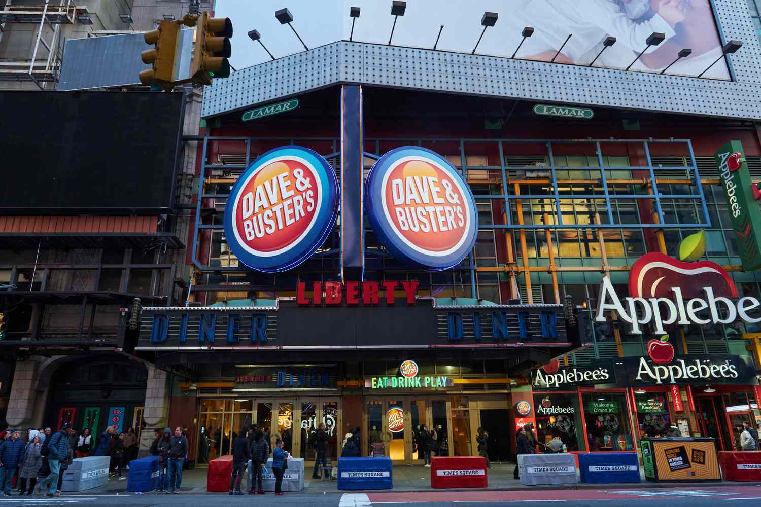 The orange and blue Dave And Buster's sign is seen above people walking on the street along Times Square.