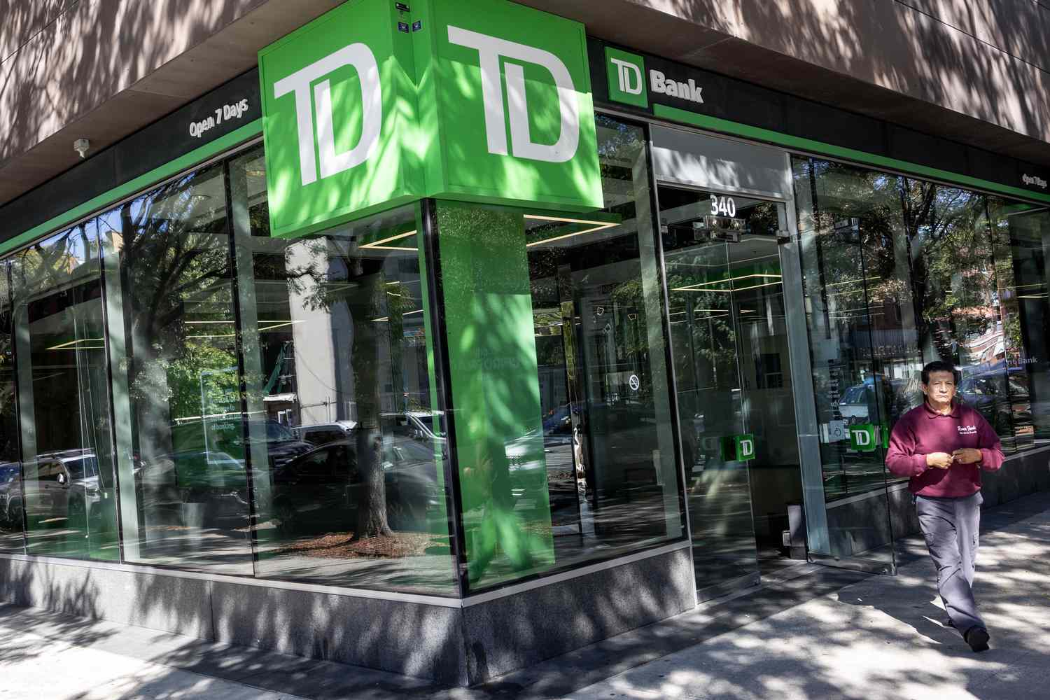 A person is seen walking outside a Toronto-Dominion Bank branch, with the bank's large green TD logo on the corner of the building.