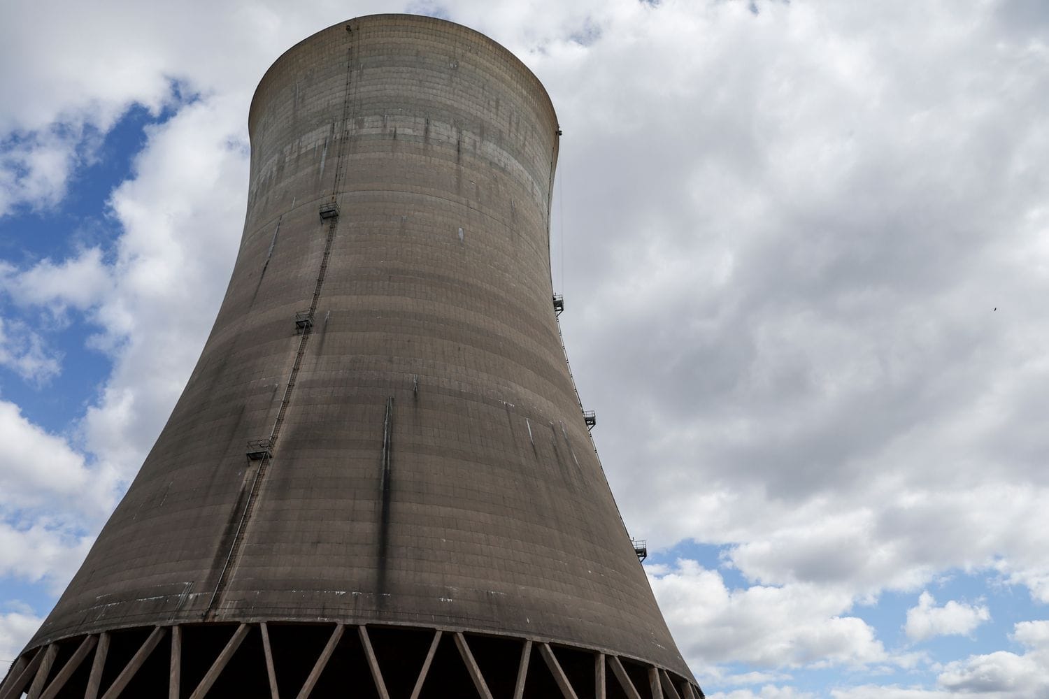 A nuclear power plant cooling tower is seen in front of a blue sky with clouds.