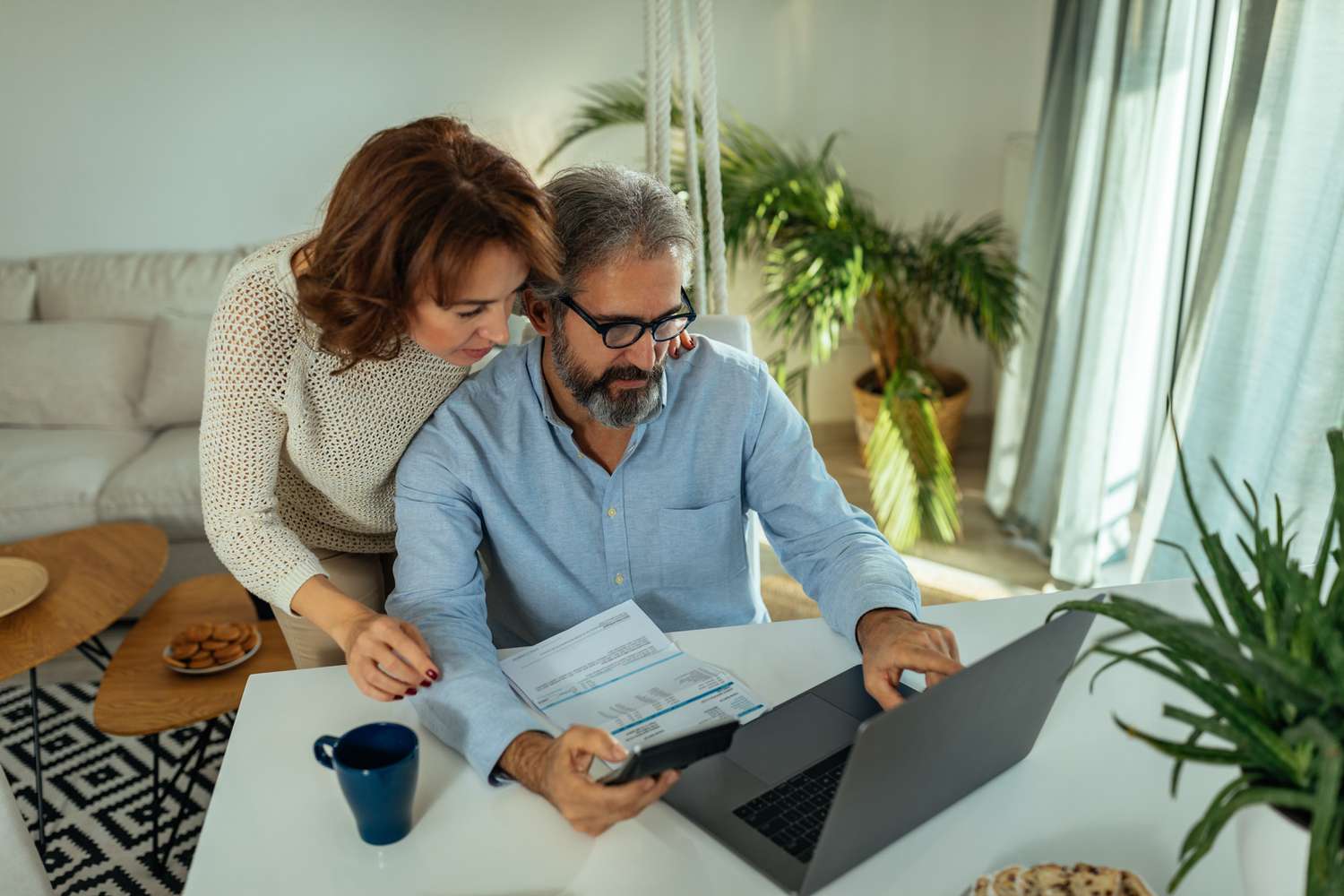 couple using laptop while sitting at the table in the living room and going through paperwork