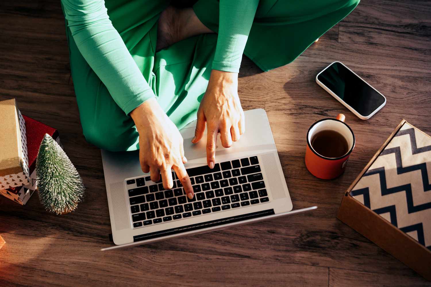 An image of a woman sitting on the floor of a home using a laptop computer. 