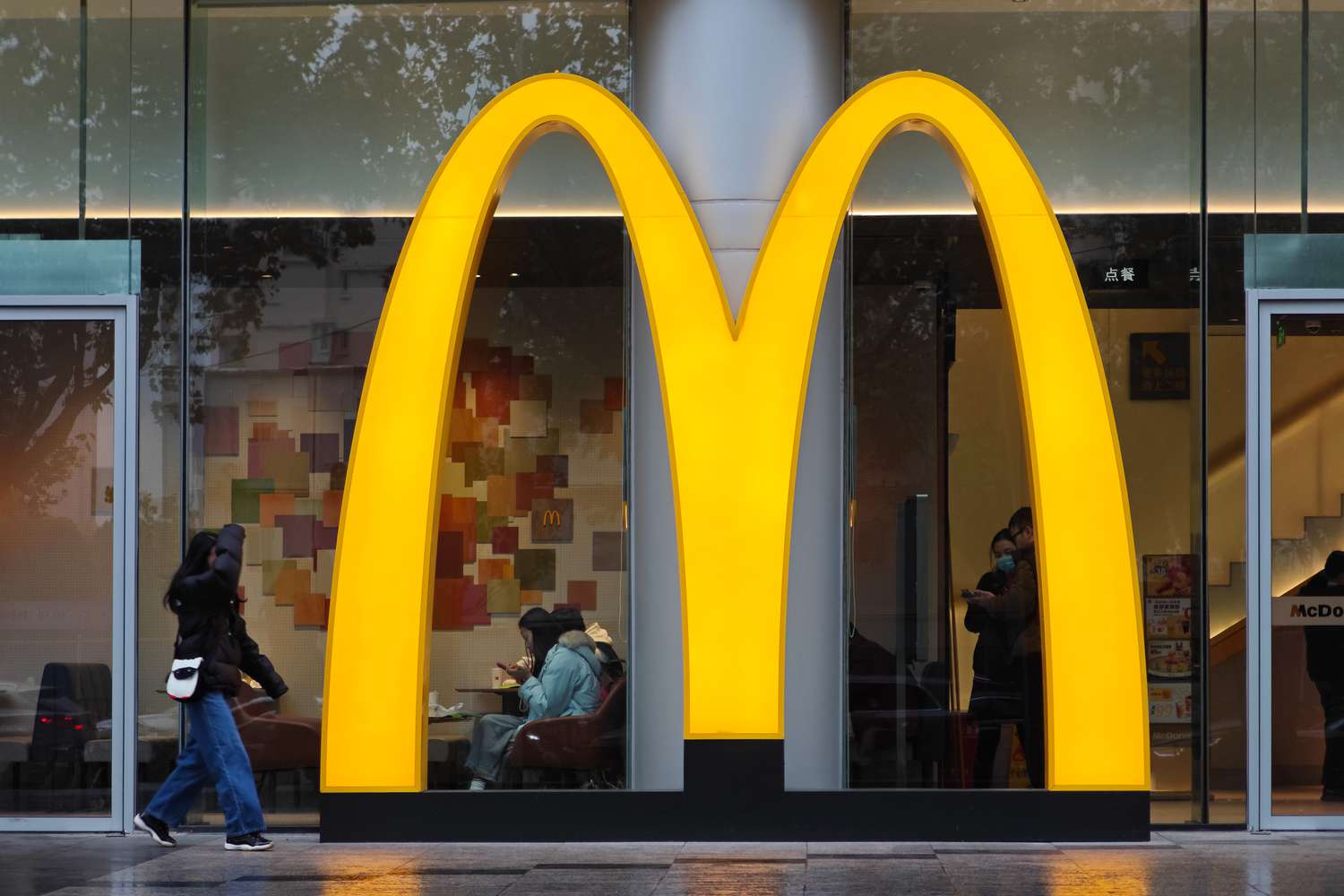 People walk and sit near the McDonald's Golden Arches logo outside a restaurant.