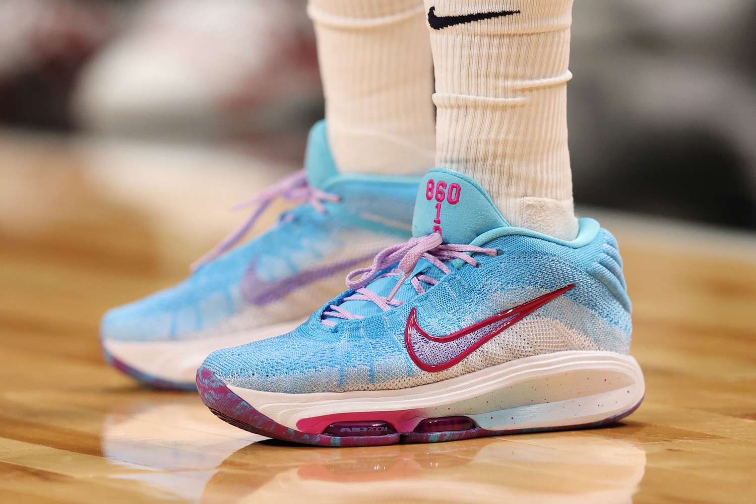 A pair of blue, white, purple, and pink Nike basketball shoes are seen on a basketball court.