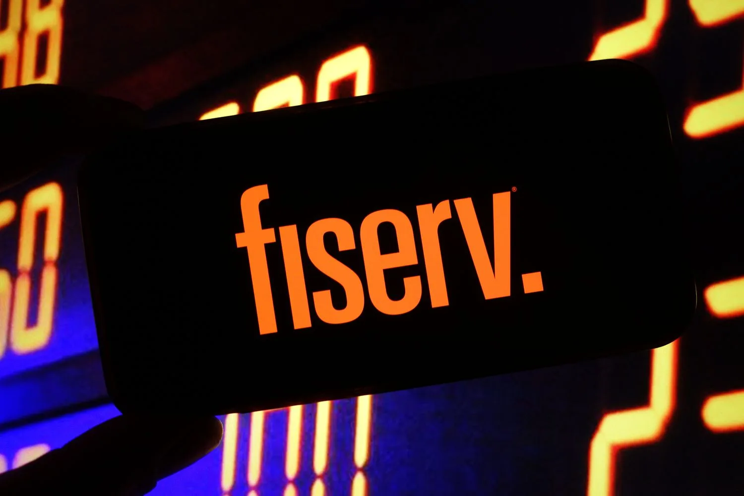 The orange Fiserv logo is seen on a phone screen in front of a black background with several orange numbers.