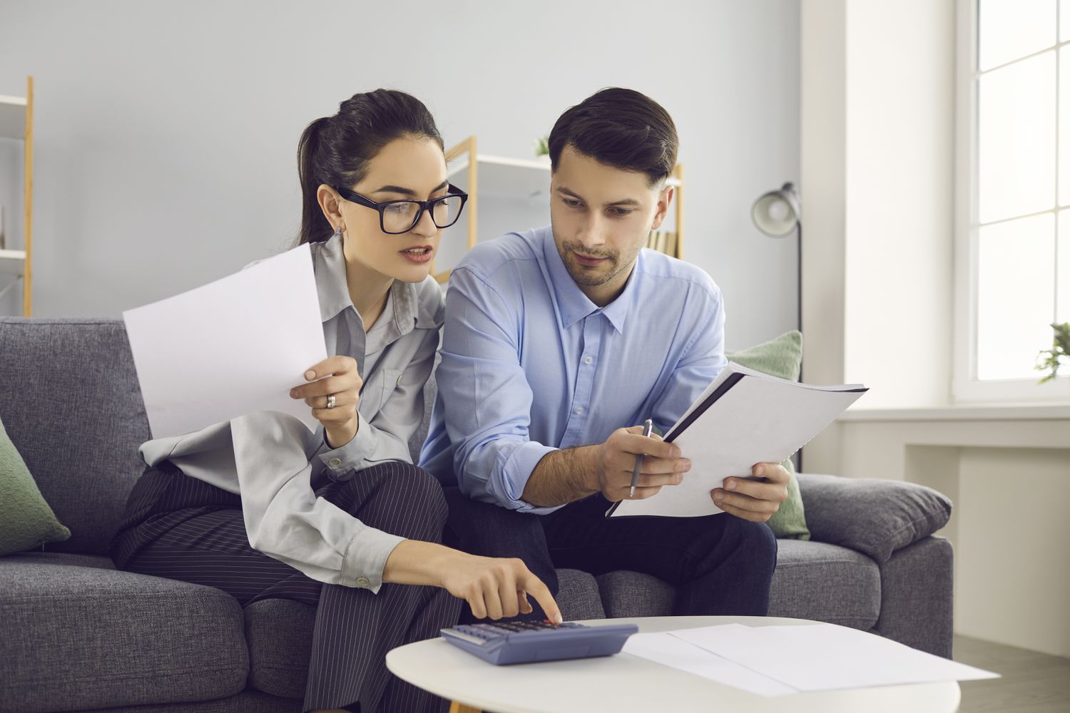 Young professional couple sitting on their sofa and looking together at documents and a calculator