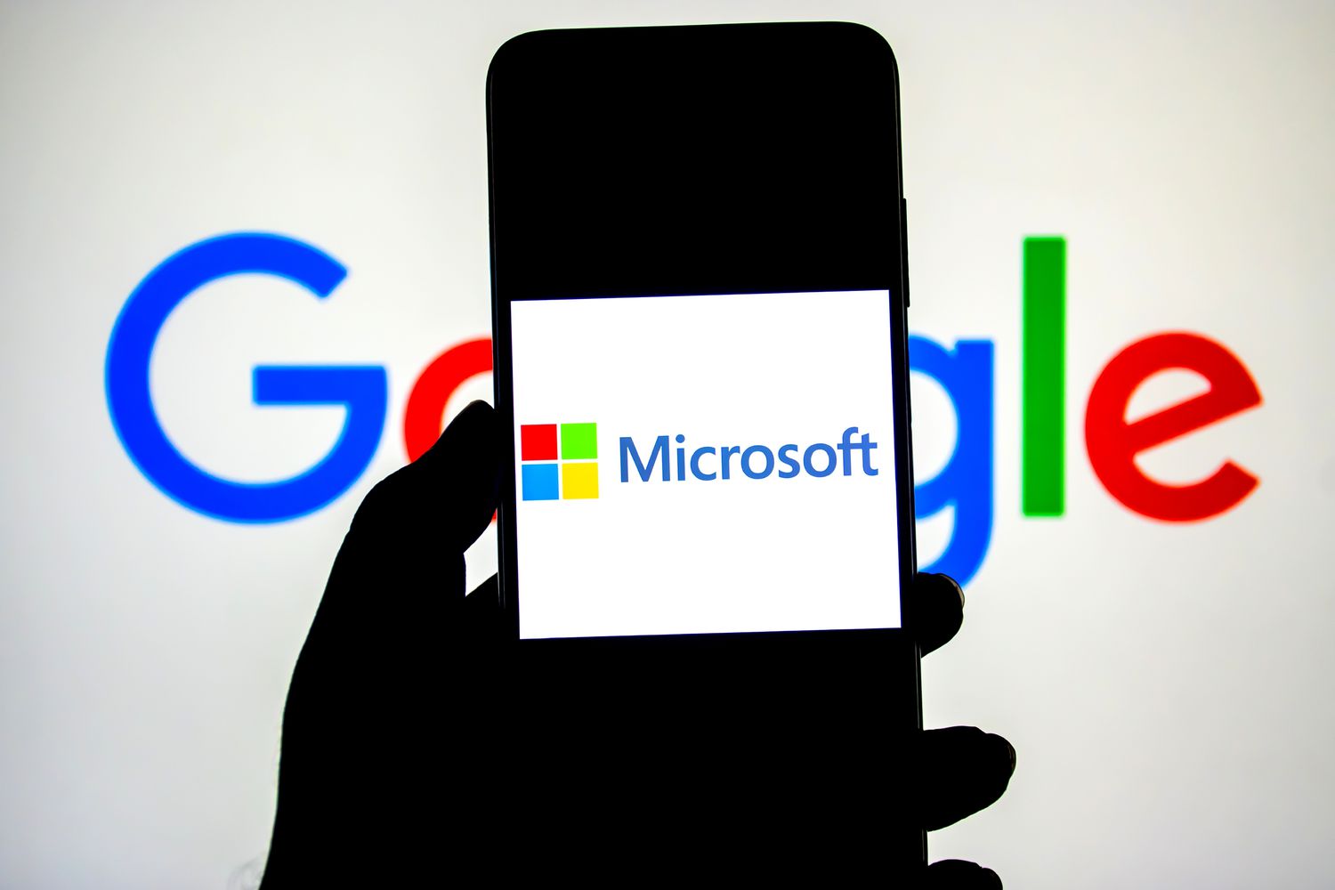 A Microsoft logo seen displayed on a smartphone with a Google logo in the background