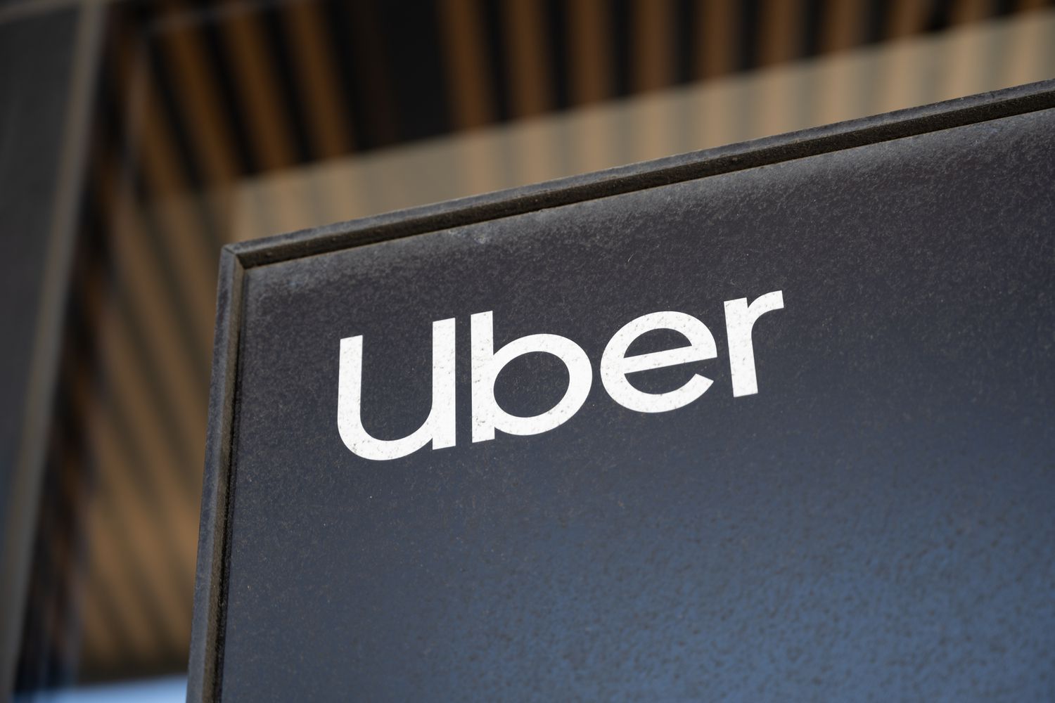 The Uber logo is seen on a black sign in front of an office building window.