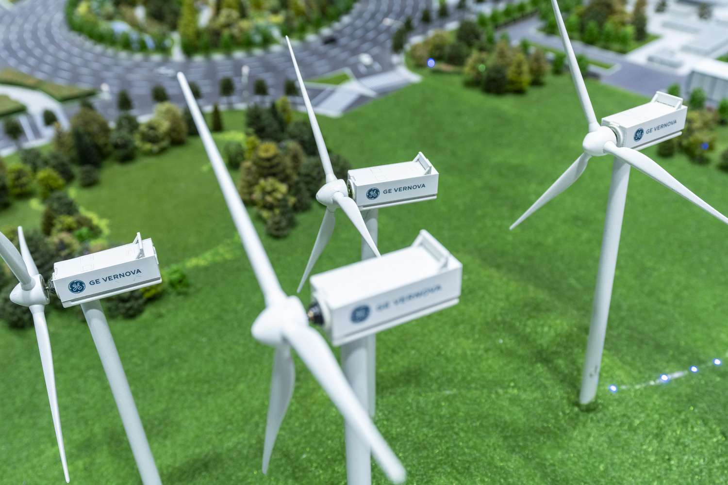 A display model shows four small wind turbines in a field surrounded by grass and trees.